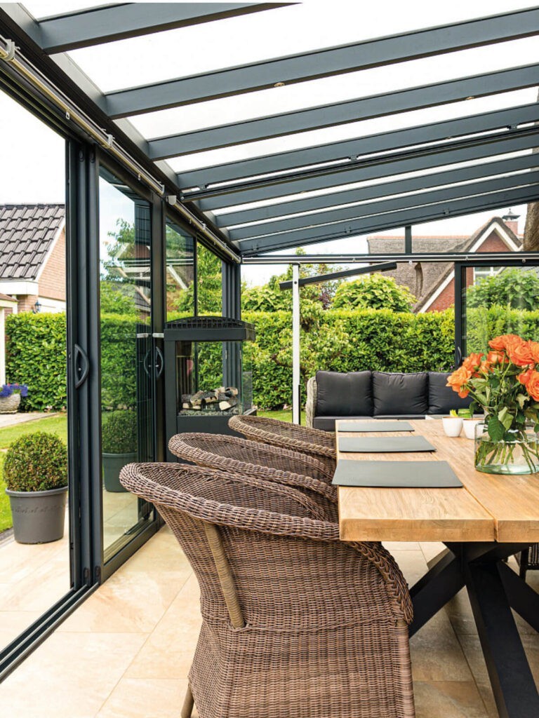 Innenansicht eines möblierten Sommergartens mit Glastüren, Esstisch und Rattan Stühlen